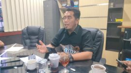 Pria berbaju batik berbicara di ruang rapat.