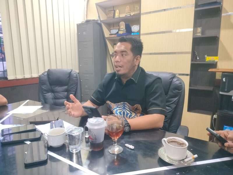 Pria berbaju batik berbicara di ruang rapat.